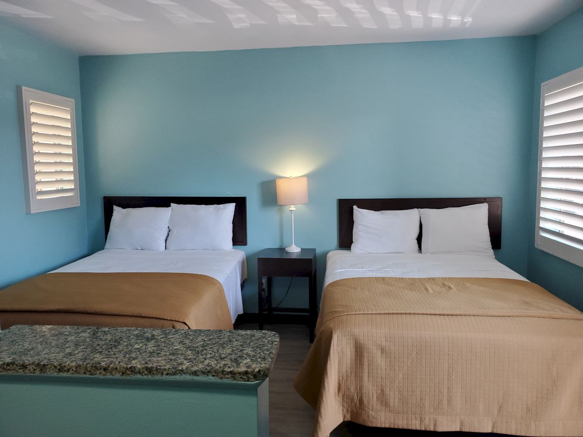 The image shows a hotel room with two beds, a nightstand with a lamp, and blue walls with white window shutters, ending the sentence.